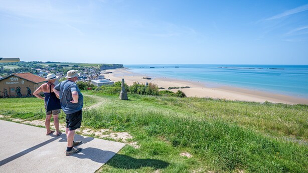 A coastal view with a paved path, grassy areas, and a beach in the background.
