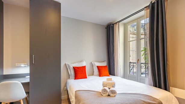 A modern hotel room with a large bed, two red pillows, a neatly made bed with towels, a desk, and a window with curtains. - La Suite de la Craffe - Vieille ville de Nancy (Nancy)