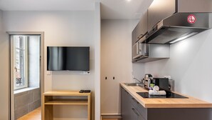 A modern kitchen with a built-in stove, a sink, and a flat-screen TV mounted on the wall. - La Suite de la Craffe - Vieille ville de Nancy (Nancy)