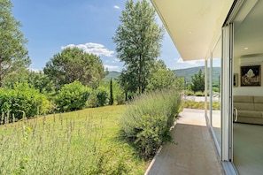 A modern house with a glass door leading to a patio, surrounded by lush greenery and a clear sky. - Apartment 2 with Lake View (Alvignano)