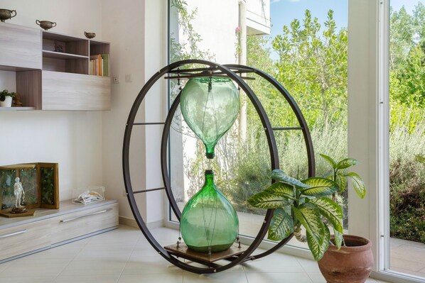 Ein Zimmer mit einem großen Fenster, einer grünen Vase auf einem Podest, einer Topfpflanze und einem Bücherregal.