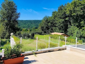 Eine Terrasse mit Blick auf eine grüne Landschaft, einem Blumentopf und einem Zaun.