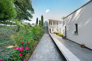 A pathway leading to a modern building with a white exterior, surrounded by greenery and flowering plants. - Apartment 2 with Lake View (Alvignano)