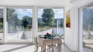 A dining area with a table set for four, large windows, and a view of greenery and hills. - Apartment with Terrace and Lake View (Alvignano)