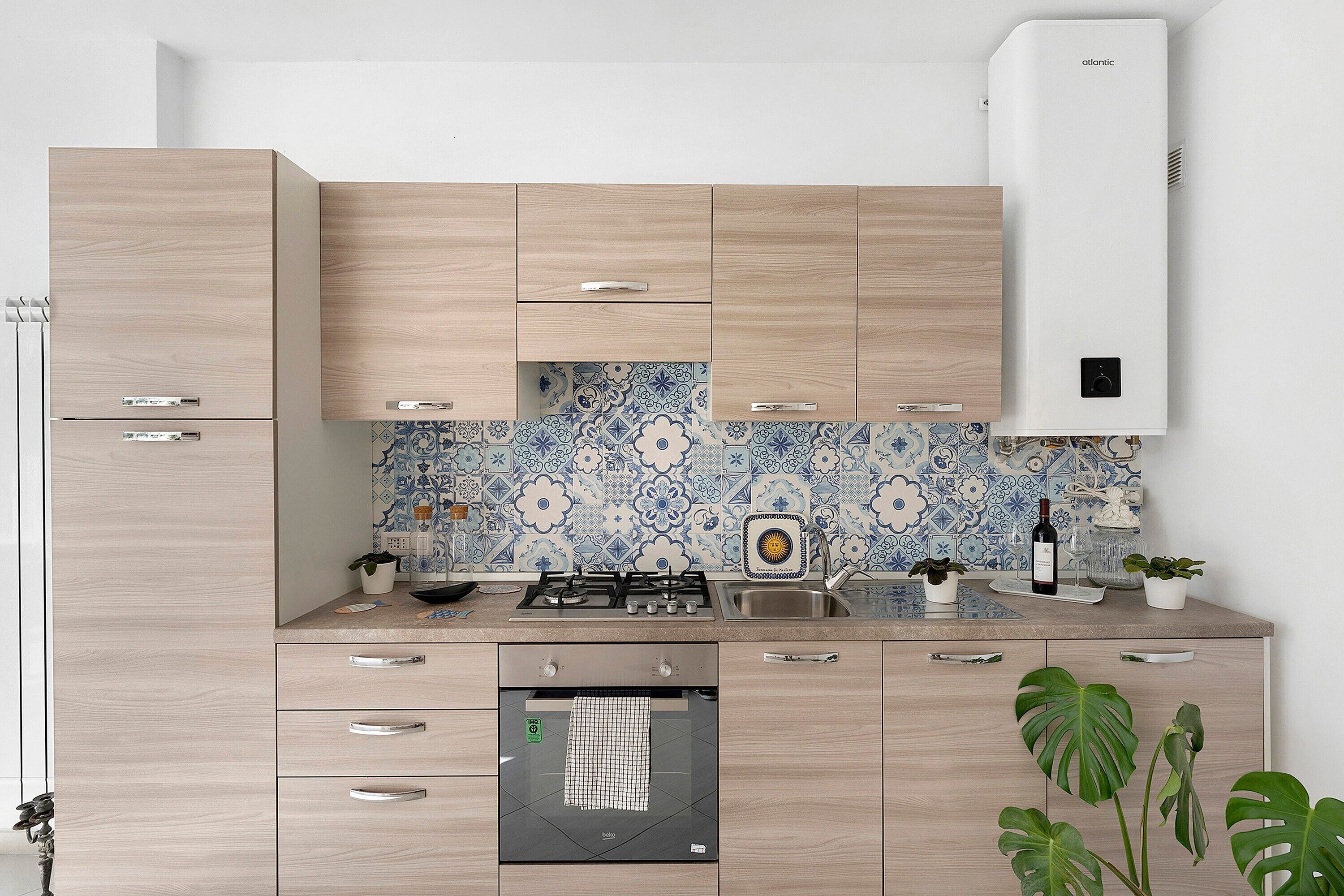 Eine moderne Küche mit hellen Holzschränken, einem eingebauten Backofen und einer gemusterten Spritzschutzwand.