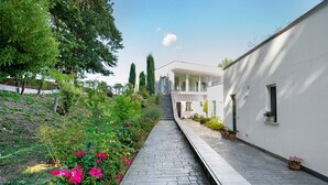 A pathway leading to a modern building with a white exterior, surrounded by greenery and flowering plants. - Apartment with Terrace and Lake View (Alvignano)
