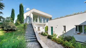 A modern house with a paved pathway, a staircase, and a garden with various plants. - Apartment with Terrace and Lake View (Alvignano)