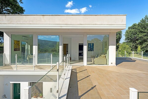 Une maison moderne dotée d’une façade en verre, d’un balcon et offrant une vue sur le paysage environnant.