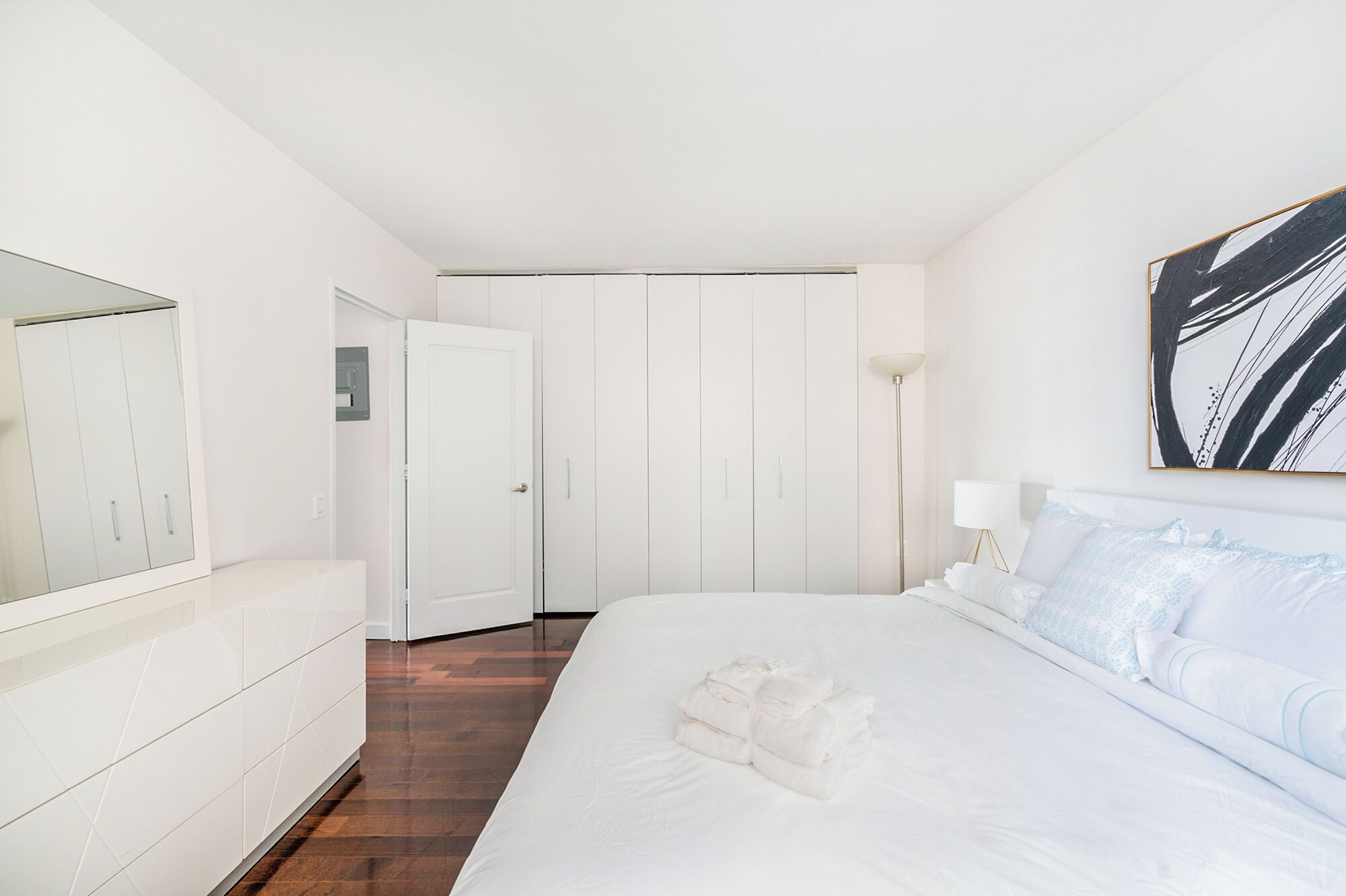 Habitación de hotel con cama, armario, puerta y un cuadro en la pared.