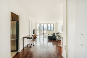 A modern apartment with a kitchen, dining area, and living room, featuring a large window with a city view. - NYC Luxe Rentals  (New York)