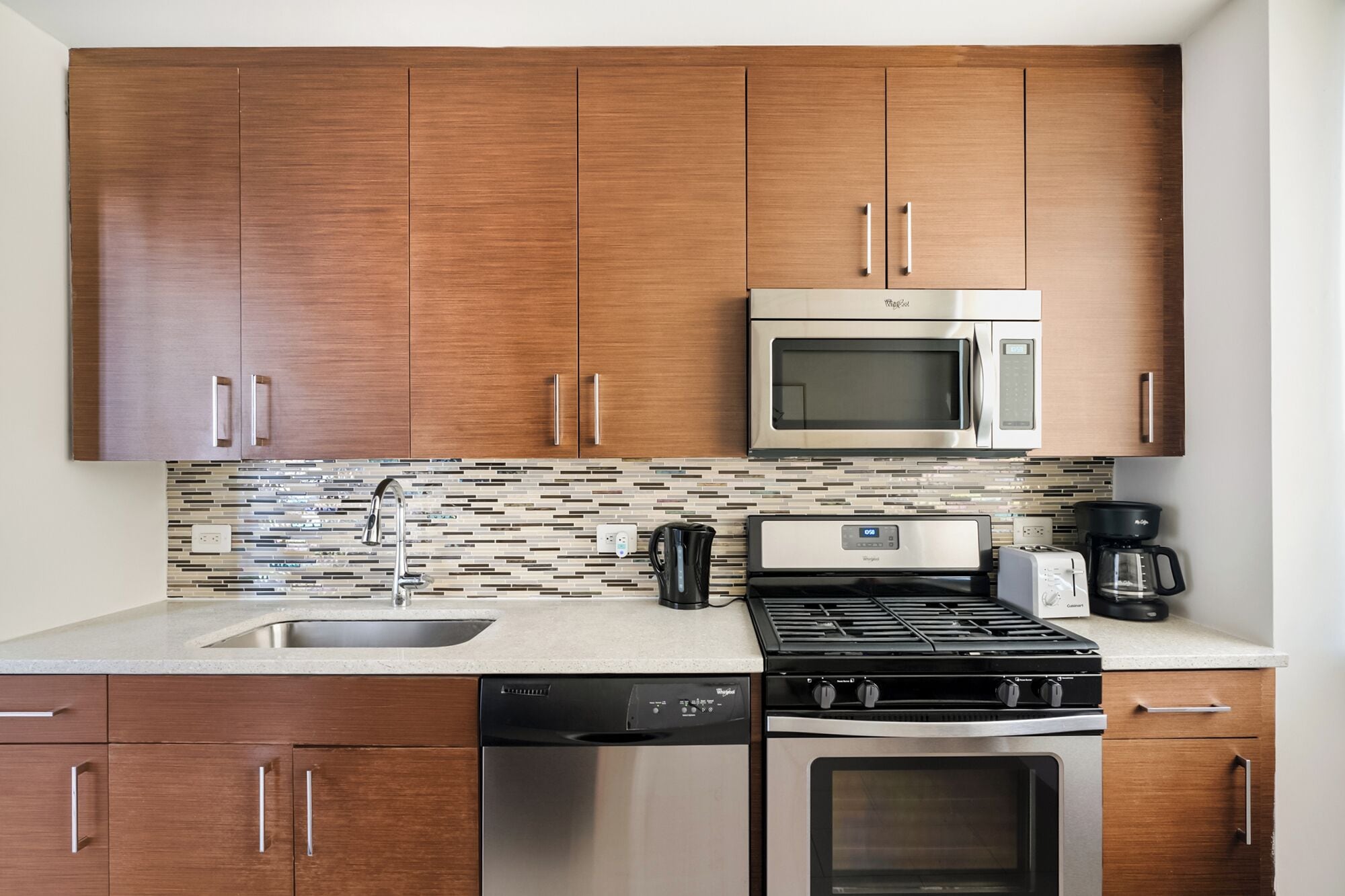 A modern kitchen with wooden cabinets, a stainless steel microwave, a gas stove, a dishwasher, and a coffee maker.