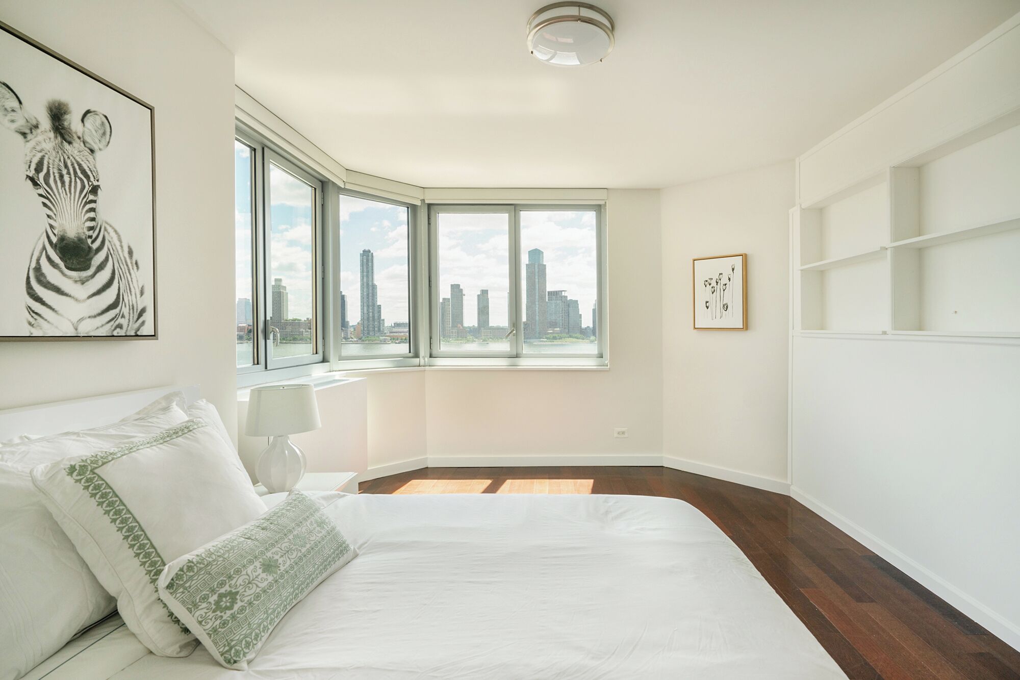 Une chambre avec un grand lit, une vue sur la ville à travers une fenêtre d’angle, une œuvre d’art représentant un zèbre accrochée au mur et un tableau encadré.