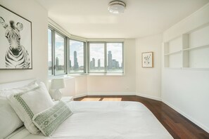 A bedroom with a large bed, a city view through a corner window, a zebra artwork on the wall, and a framed picture on the wall. - NYC Luxe Rentals  (New York)