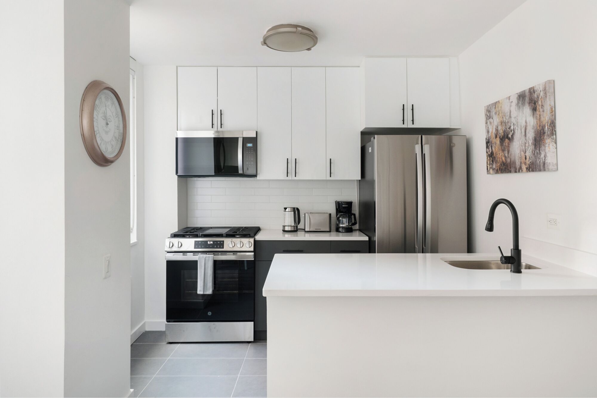 Una cucina moderna con mobili bianchi, elettrodomestici in acciaio inossidabile, forno, microonde e frigorifero.