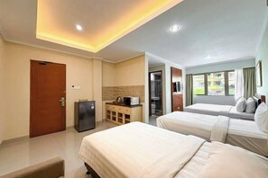 A hotel room with two beds, a desk with a computer, a refrigerator, and a view of the outside. - Svarna Hotel (Bali)
