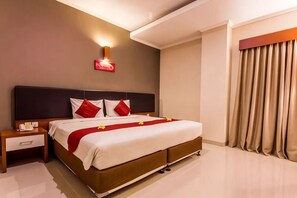 A hotel room with a bed, nightstand, and a wall-mounted light fixture. - Svarna Hotel (Bali)