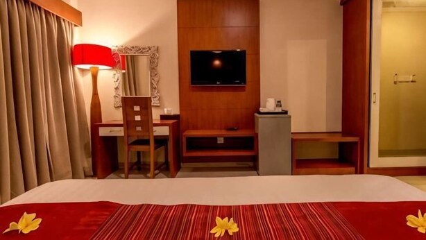 A hotel room with a bed, a desk, a chair, a television mounted on the wall, and a sliding door. - Svarna Hotel (Bali)