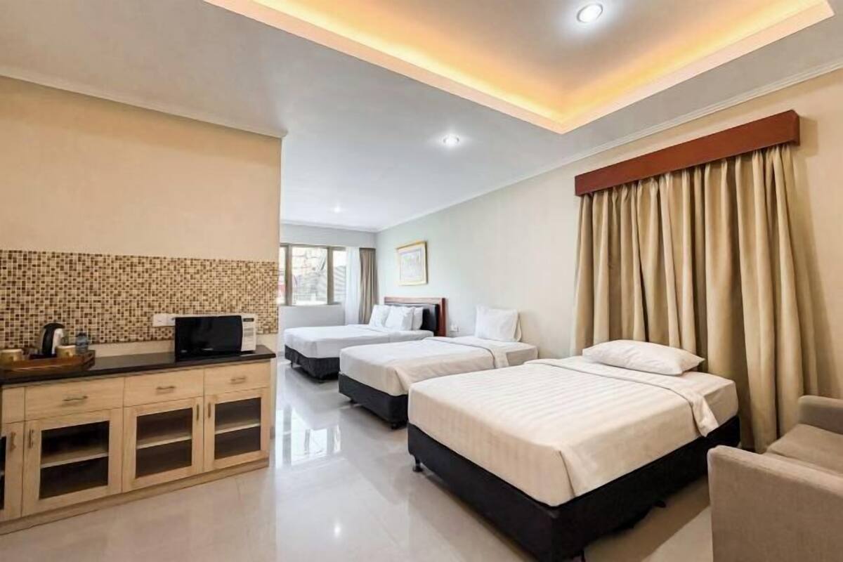 A hotel room with three beds, a kitchenette, a TV, and a large window with curtains.