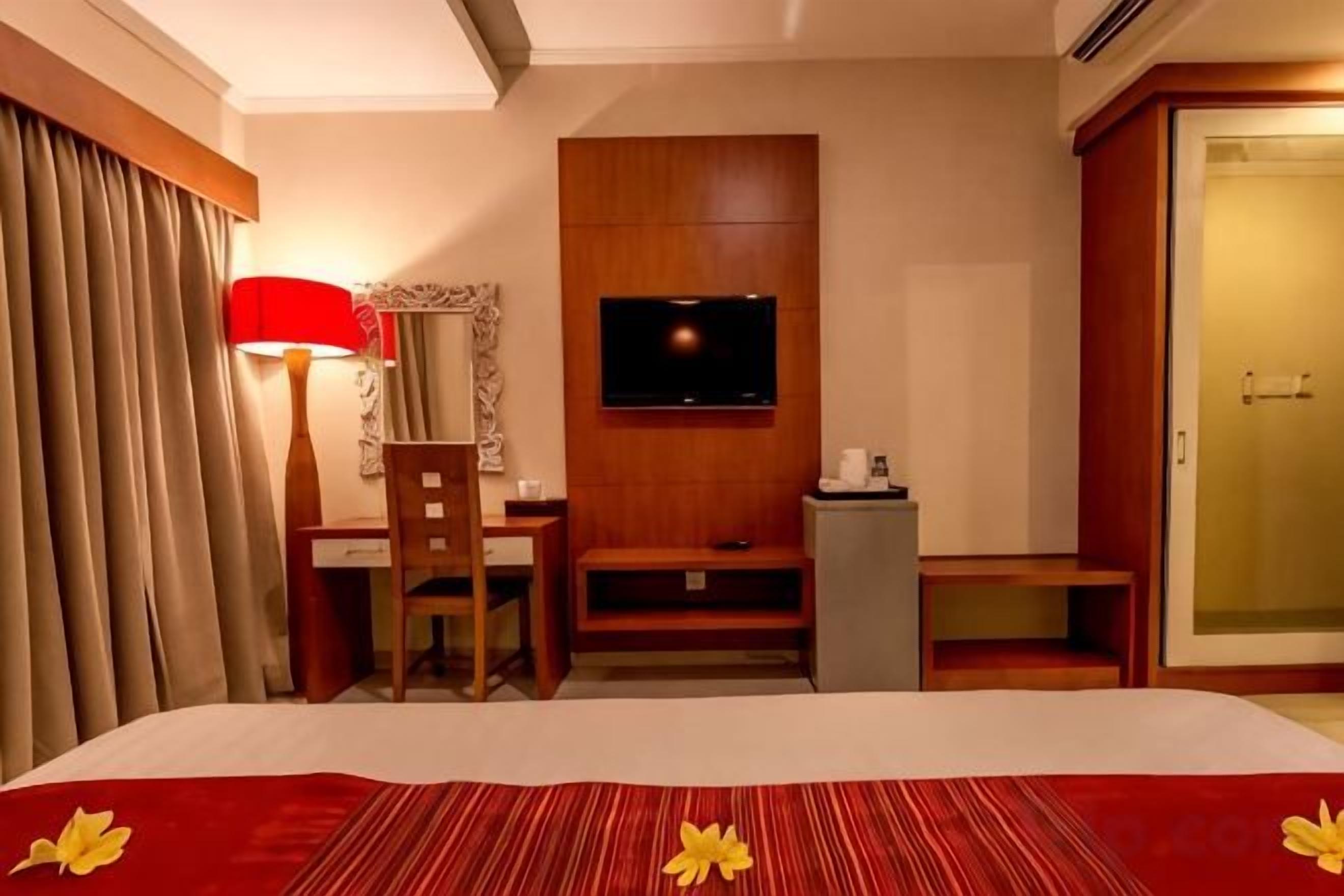 A hotel room with a bed, a desk, a chair, a television, and a wardrobe.