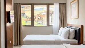 A hotel room with two beds, a TV, a window with curtains, and a framed picture on the wall. - Svarna Hotel (Bali)