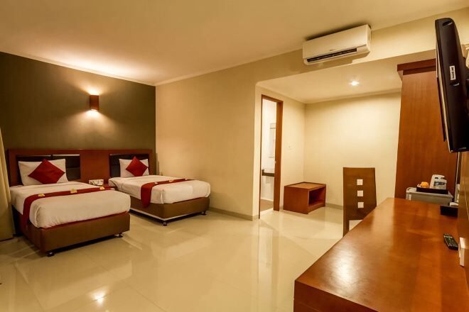 Habitació d'hotel amb dos llits, una taula de nit de fusta, televisió i aire condicionat.