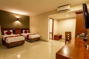 A hotel room with two beds, a wooden desk, a TV, and an air conditioning unit. - Svarna Hotel (Bali)