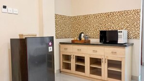 A kitchenette with a refrigerator, microwave, wooden cabinet, and tiled backsplash. - Svarna Hotel (Bali)