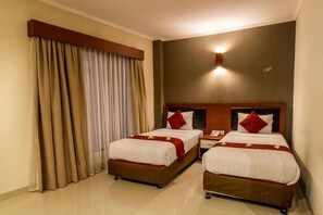 A hotel room with two beds, a nightstand, and a wall-mounted lamp. - Svarna Hotel (Bali)