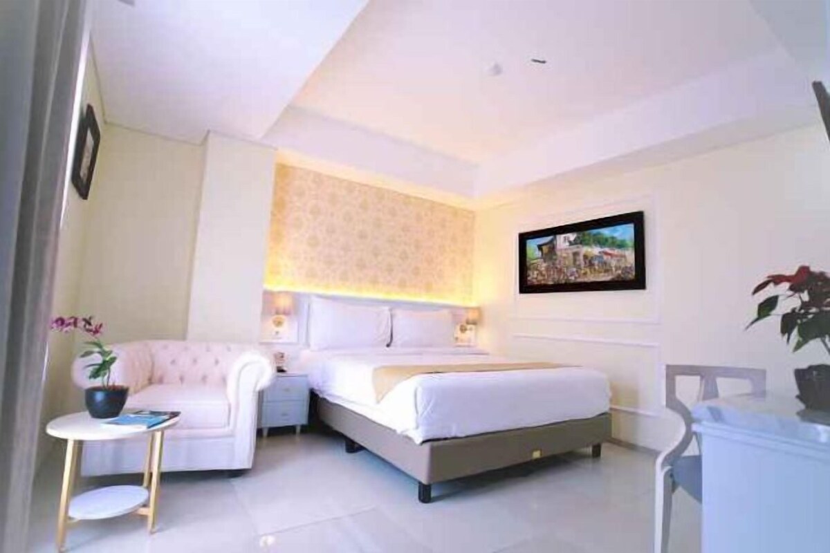 A bedroom with a bed, bedside table, chair, and a small table with a plant.