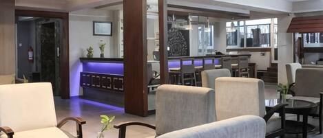 A hotel lobby with seating areas, a reception desk, and a bar/lounge area.