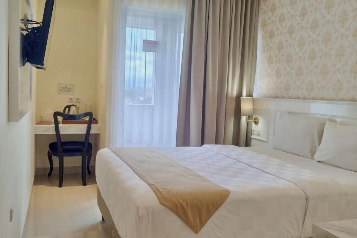 Een hotelkamer met een bed, een bureau, een stoel en een raam met gordijnen.