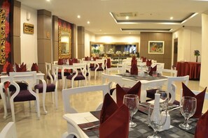 A dining area with round tables and white chairs, a buffet in the background, and a chandelier. - The Cube Hotel Malioboro, Azana Hotels Collection (Mantrijeron)