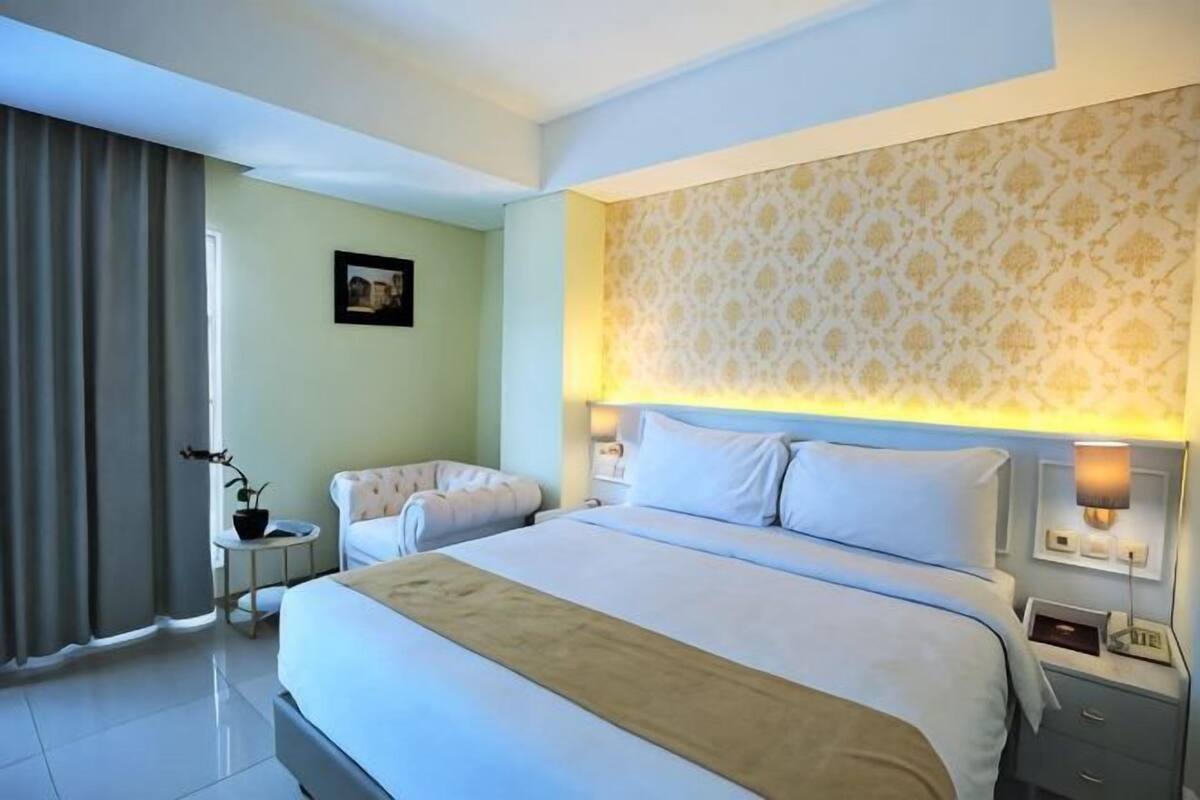 Een hotelkamer met een groot bed, nachtkastjes, een lamp en een raam met gordijnen.