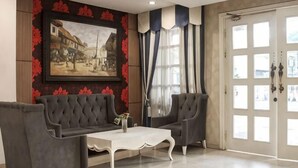 Une pièce comprenant un canapé, des fauteuils, une table basse, un tableau accroché au mur et une porte avec des panneaux de verre.