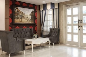 A room with a sofa, armchairs, a coffee table, a painting on the wall, and a door with glass panels. - The Cube Hotel Malioboro, Azana Hotels Collection (Mantrijeron)