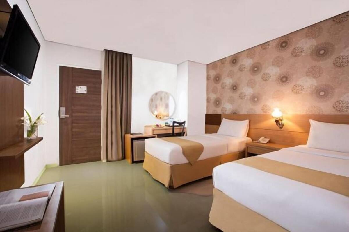 Een hotelkamer met twee bedden, een bureau, een televisie en een grote spiegel.