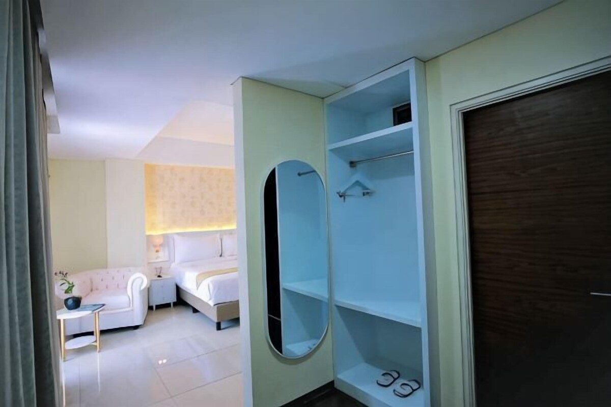 Une chambre d’hôtel avec un lit, une salle de bain avec un miroir et des étagères, et une porte.