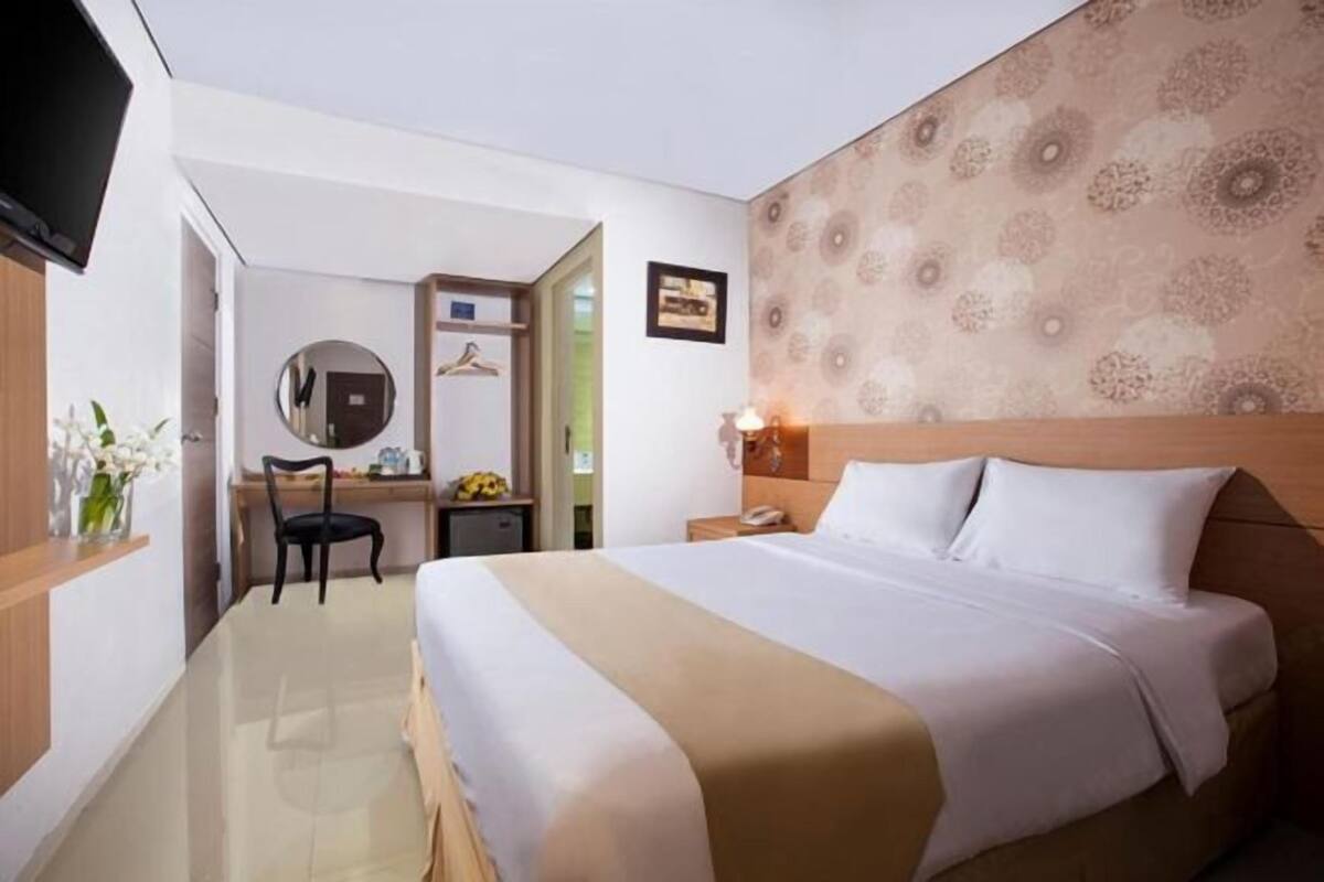 Hotelkamer met een bed, bureau, stoel, spiegel, televisie en een wand met een decoratief patroon.