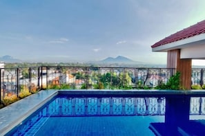 A rooftop pool with a metal railing, a view of distant mountains, and a clear sky.