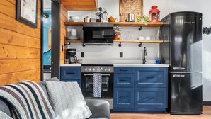 A modern kitchen with a microwave, oven, and refrigerator, wooden walls, and a cozy seating area with a blanket. - Grizzly Bear Cabin # 2. (Central Kootenay)