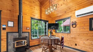 A wooden cabin interior with a fireplace, dining table, chairs, and a TV mounted on the wall. - Grizzly Bear Cabin # 2. (Central Kootenay)