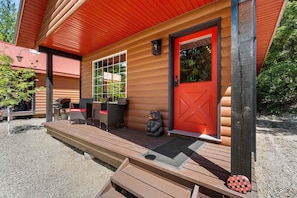 Une cabane en bois avec une porte rouge, une véranda avec un banc et une petite statue d’ours.