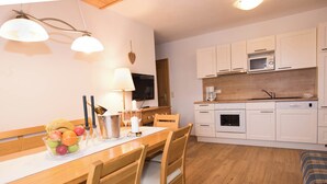 Una cucina moderna con mobili bianchi, un forno a microonde e una macchina da caffè. C'è un tavolo da pranzo con sedie e una ciotola di frutta.