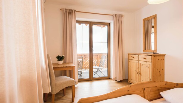 Una camera da letto con un letto in legno, una scrivania, una sedia e un balcone con vista.