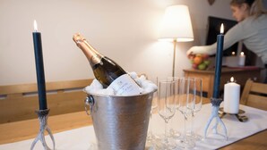 Un secchio di metallo con una bottiglia di champagne e ghiaccio, circondato da bicchieri da vino vuoti e candele su un tavolo.