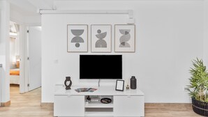 Un salon moderne avec un meuble de rangement blanc pour l’équipement audiovisuel, un téléviseur à écran plat et trois œuvres d’art abstraites accrochées au mur.