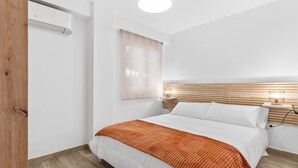 Une chambre à coucher comprenant un lit, une tête de lit en bois, une table de chevet avec une lampe et un climatiseur fixé au mur.