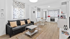 Un appartement moderne avec un canapé en cuir noir, une table à manger blanche et un coin cuisine.