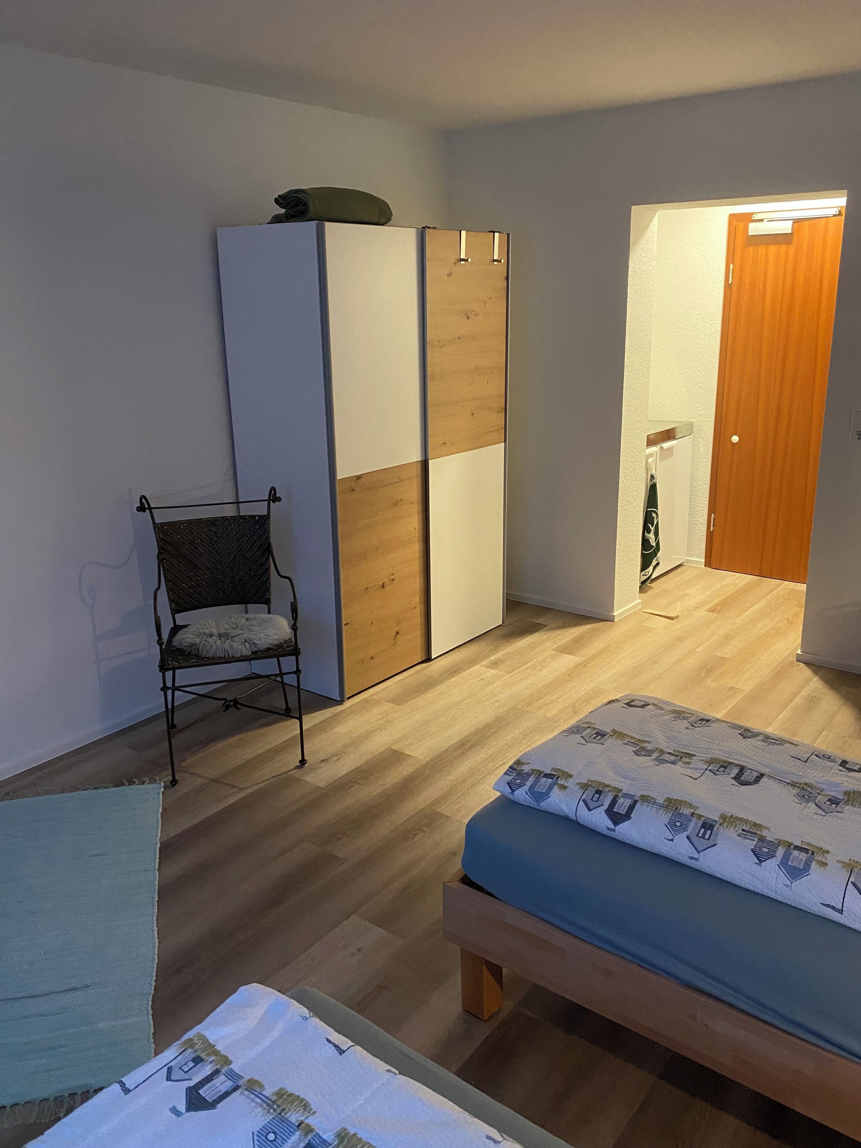 Een slaapkamer met twee bedden, een garderobe, een stoel en een houten vloer.