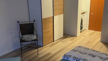 A bedroom with two beds, a wardrobe, a chair, and a wooden floor.